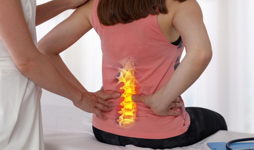 An image showing woman with lower back pain is being treated with chiropractic care. The spine is shown as a graphic on the woman’s lower back.