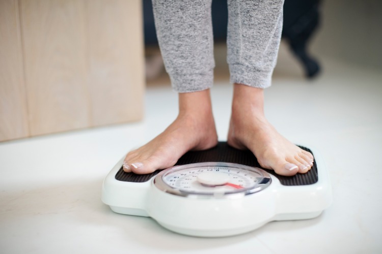 An image of a person standing on a bathroom scale to show how weight loss works to help ease back pain.