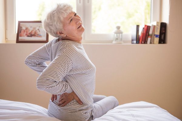 Photo of an elderly woman grasping her lower back in need of doing a search for a "local chiropractor near me".