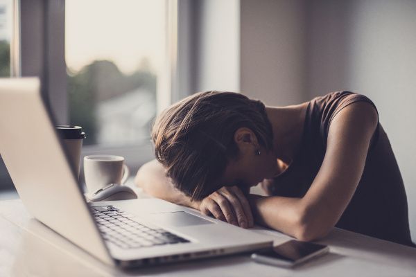 Image of a stressed woman with her head down on a desk and low back pain