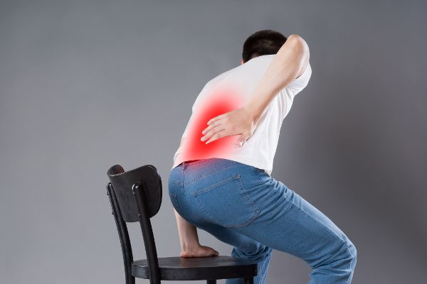 Image of a man getting out of a chair and holding his back because he needs sciatica treatment.