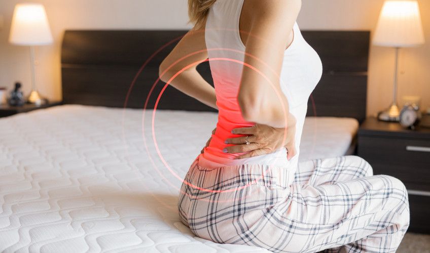 An image showing a woman sitting on a mattress with lower back pain from a herniated disc.