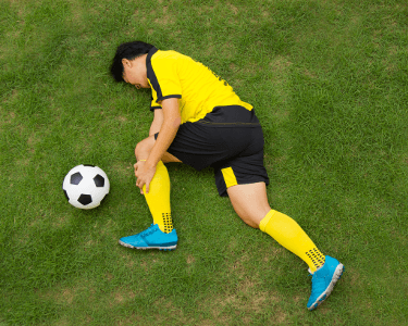 Soccer player on ground holding knee in pain.