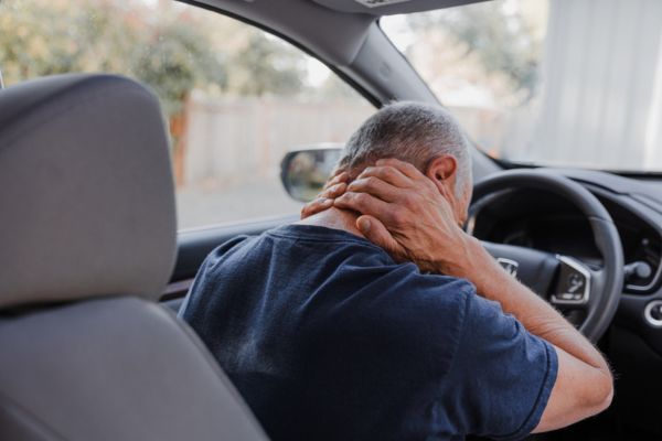 A man sits in his car and holds his neck