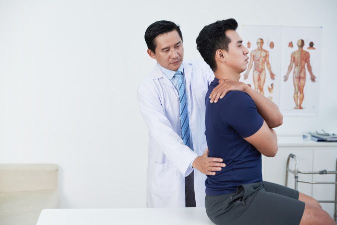 An image showing a chiropractor examining a patient sitting on a table with his arms folded. 