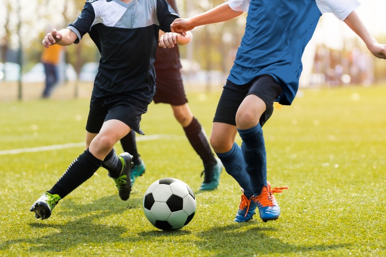 An image of two soccer players running and kicking a soccer ball.