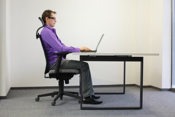 An image of a man sitting with correct posture at a computer desk. 