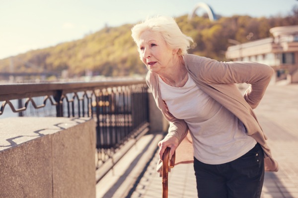 An older woman hunches over with back pain