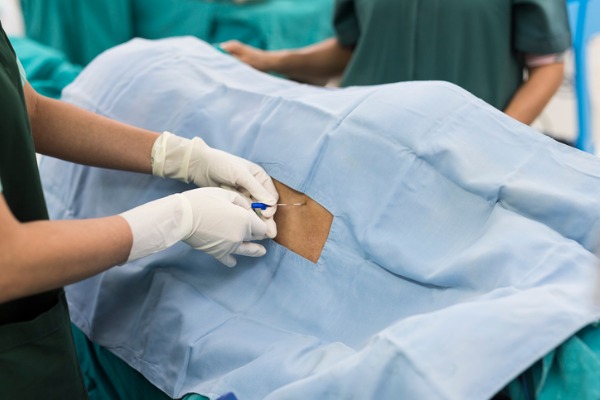 A doctor performs an epidural injection on a patient laying on a table