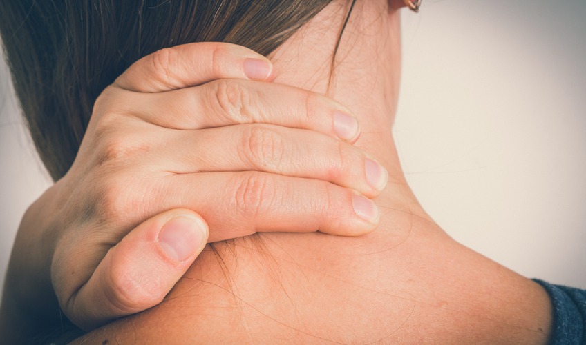 A woman at her computer holds her neck while it hurts.