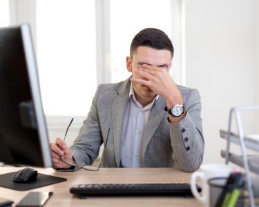 Man at desk rubs his eyes because of a headache