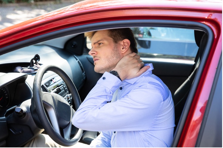 An image of a man inside of a car holding his neck in pain, which is one of the signs of whiplash.