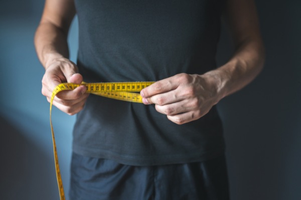 An image of a man with a measuring tape around his waist to show weight loss and back pain relief. 