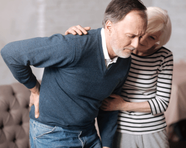 A man needing a chiropractor holds his back in pain while trying to walk