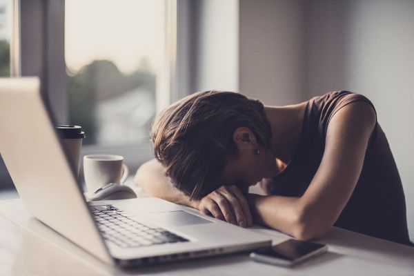 A stressed woman leans over her desk with her head on her hands