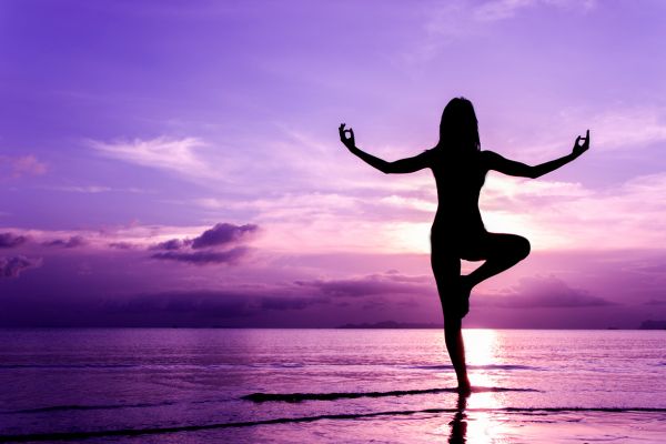 A woman does yoga on the beach in front of a sunset